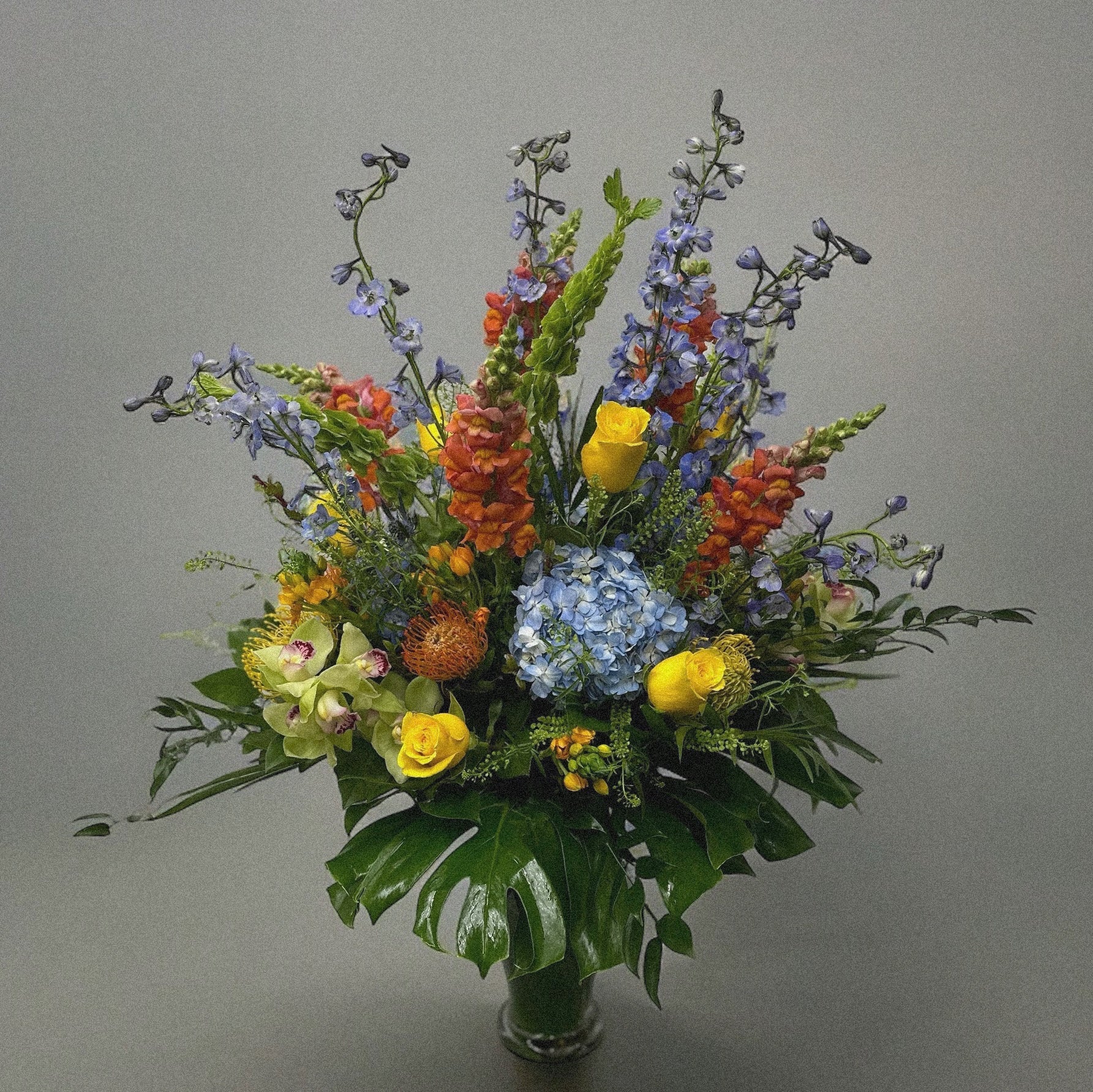 Luxury floral arrangement with lavender delphiniums, vibrant blooms, and monstera leaves. Best flower shop in Toronto, same-day delivery.