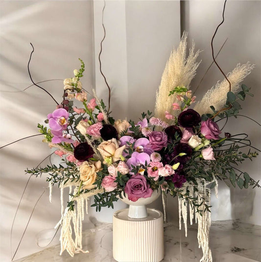  "Chic and modern floral centerpiece with delicate orchids, roses, and pampas grass – perfect for sophisticated home or event decor